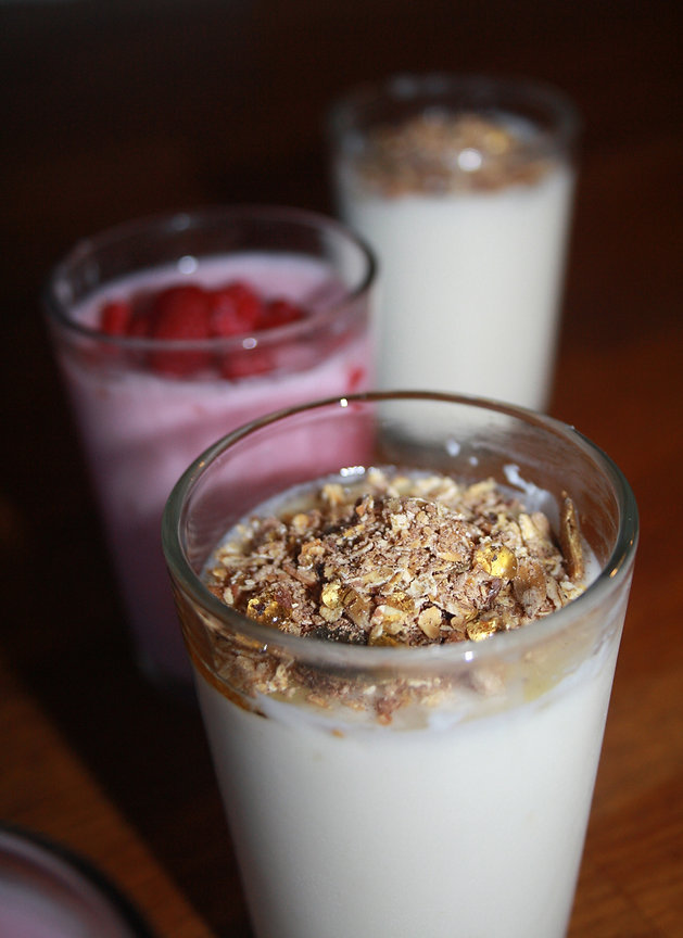 Drie glazen gelaagd zuivelvrij dessert met granola en bessen op een donkere houten tafel, warme aardetinten