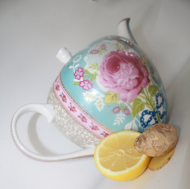 Sierlijke theepot met bloemenmotief naast een halve citroen en verse gemberwortel in pastelkleuren